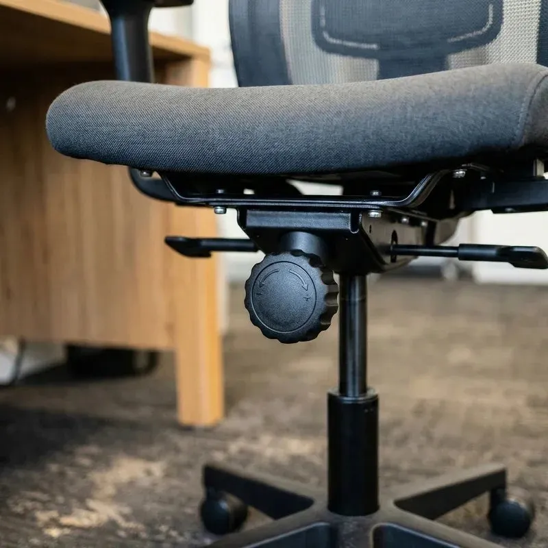 The round tilt tension knob under the seat of a grey office chair.