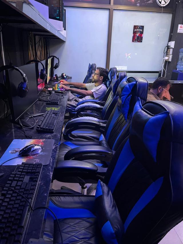 A row of gaming café chairs recovered in matching blue and black leather, with customers playing at the machines.
