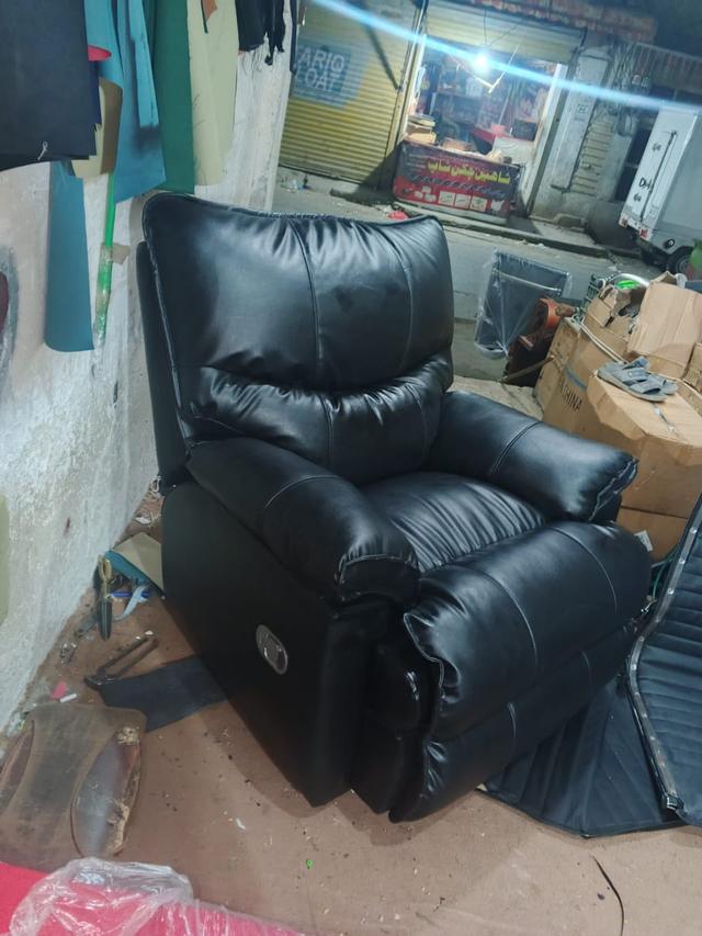 A recliner armchair finished in black leather after reupholstery, standing outside the workshop.