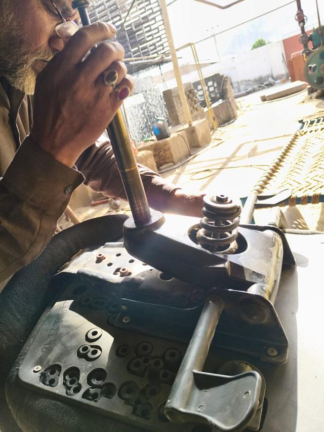 Close view of hands fitting a gas lift cylinder into a stripped office chair mechanism at a workbench.
